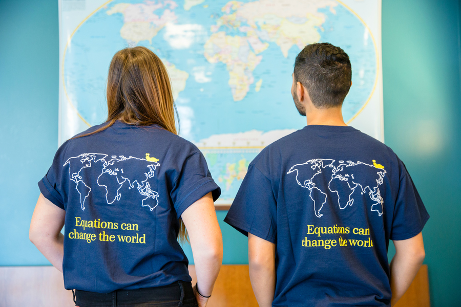 Two people looking at a map. They are wearing t-shirts that say, Equations can change the world.