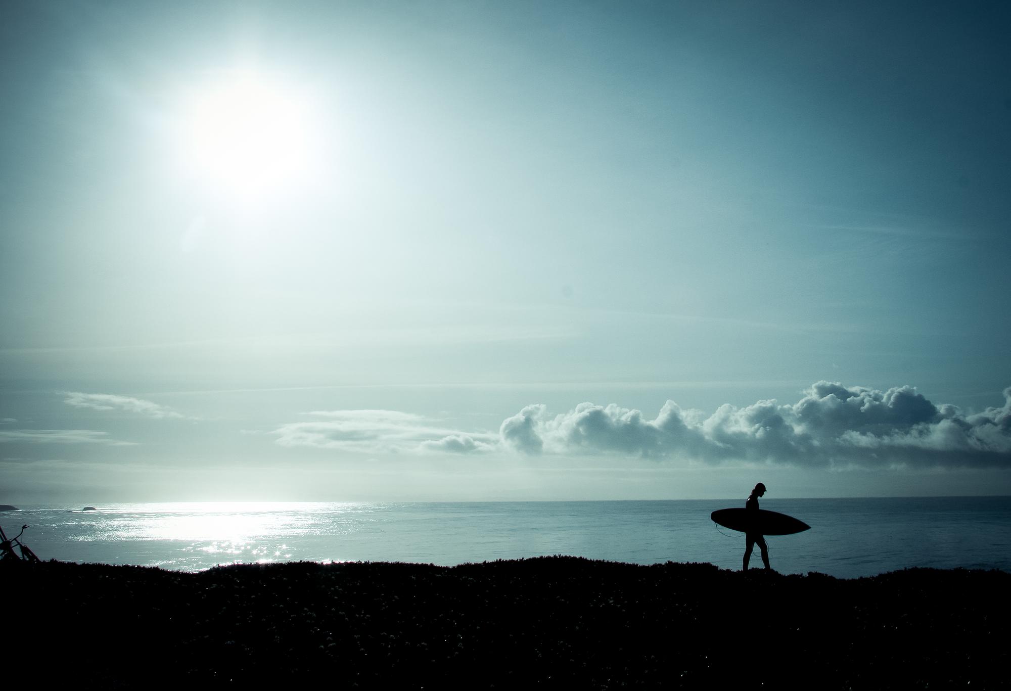 Silhouette of person walking by the ocean with a surf board