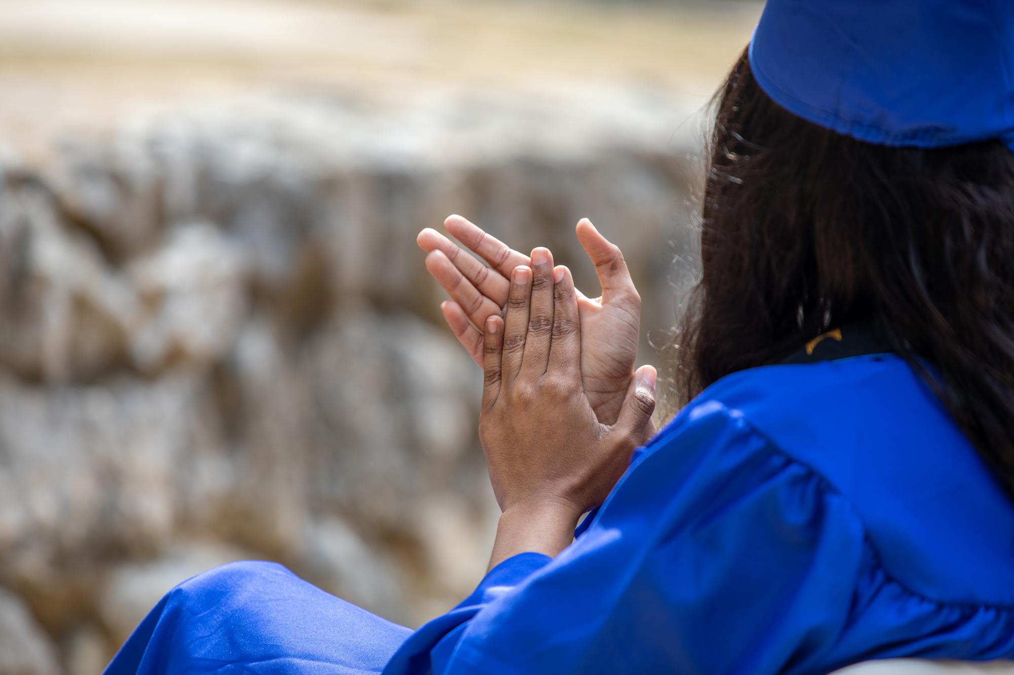 Close-up of a person clapping who is wearing a commencement gown and motarboard.