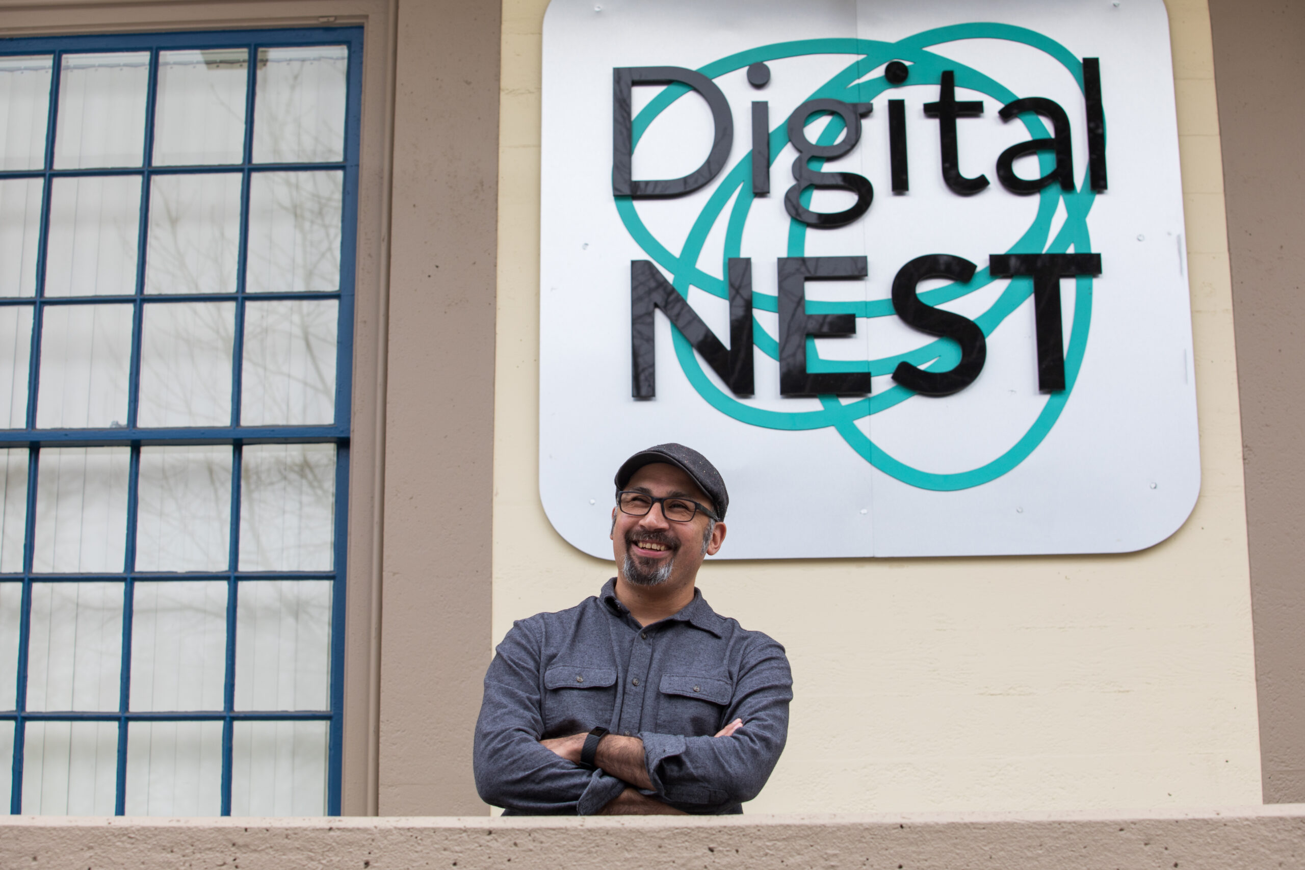 UCSC alum Jacob Martinez stands in front of the sign and building for the business he founded, Digital NEST.