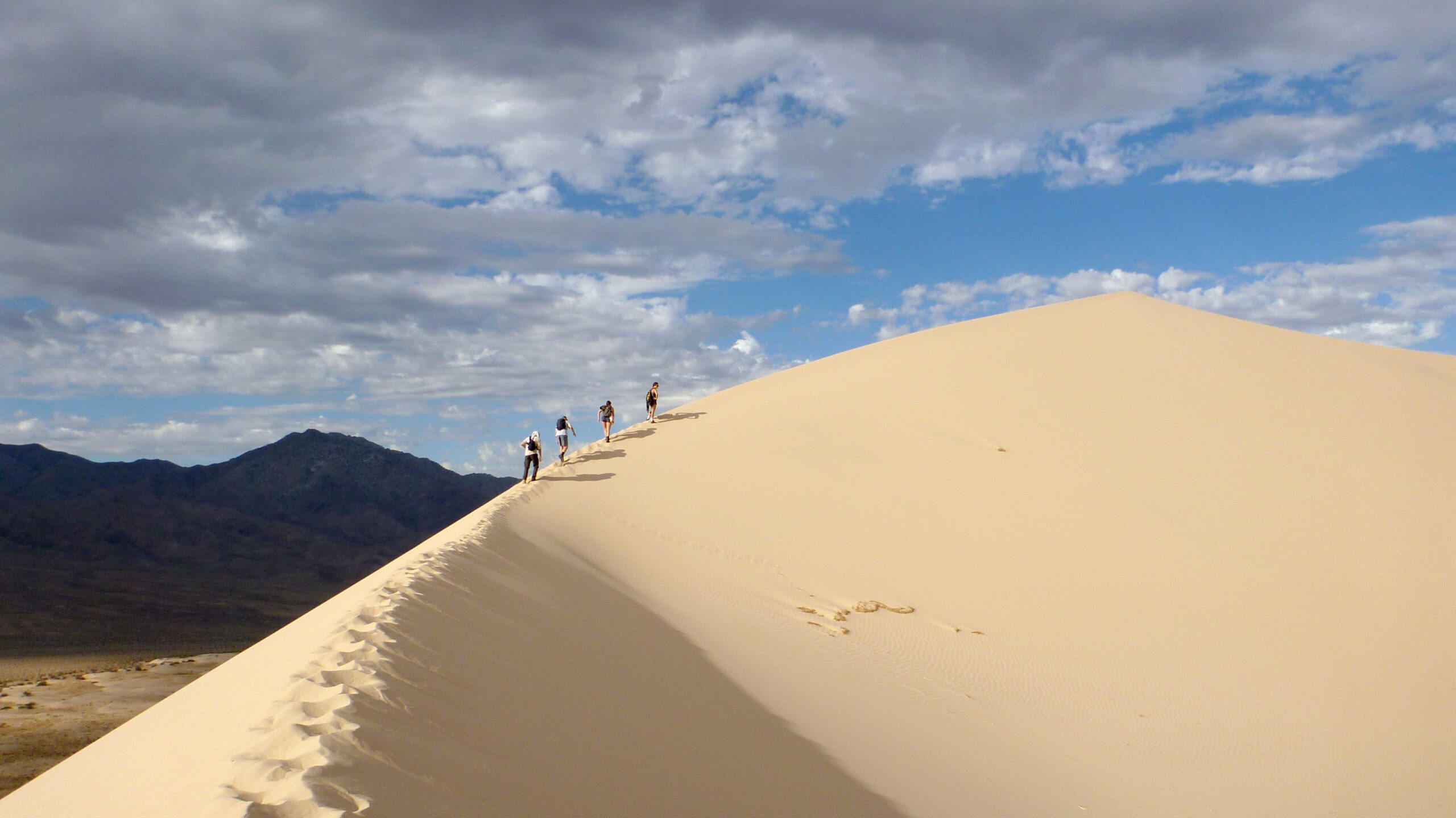 Four students hiking up a giant sand dune
