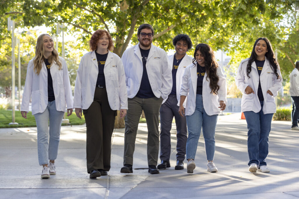 Medical students posing together outdoors in white lab coats.