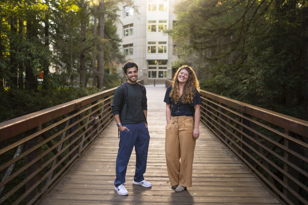 Two students standing together on a wooden bridge outdoors.