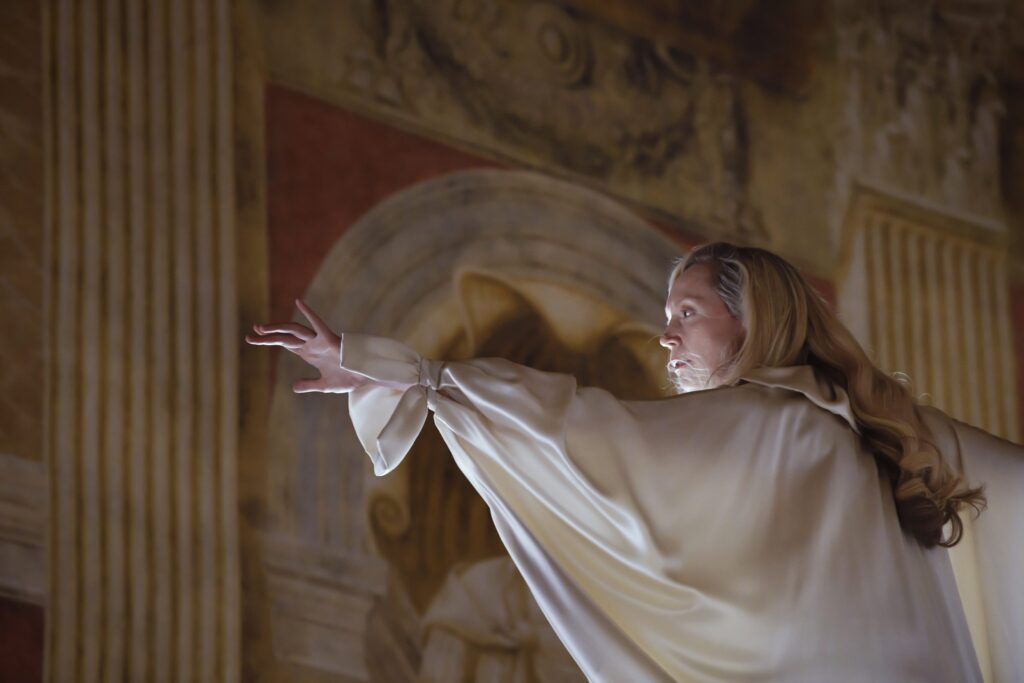 A performer in a white dress interacting with a large painting on a wall.