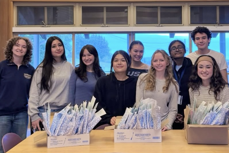 A group of student volunteers posing behind tables of packaged gifts.